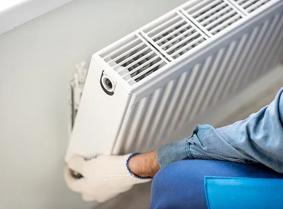 Un technicien ganté installe ou répare un radiateur de chauffage central blanc à Saint-Pathus près de Meaux en Seine-et-Marne 77