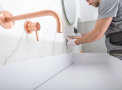 Homme installant un robinet en cuivre sur un mur de marbre blanc au-dessus d'un lavabo à Saint-Pathus près de Meaux en Seine-et-Marne 77