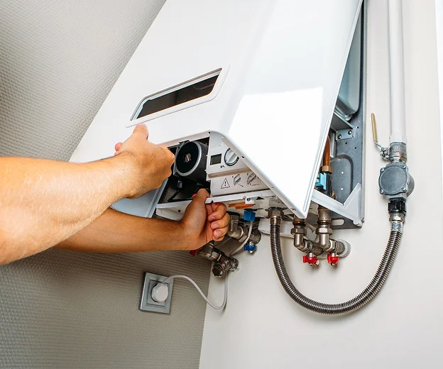 Des mains d'homme réparent un chauffe-eau mural blanc avec des tuyaux exposés à Saint-Pathus près de Meaux en Seine-et-Marne 77