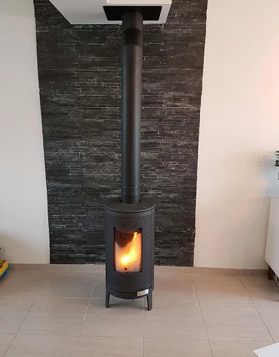 Cheminée autoportante noire avec foyer allumé devant un mur en pierre foncée à Saint-Pathus près de Meaux en Seine-et-Marne 77